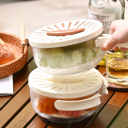 Two stacked salad spinners on a wooden table with a glass of juice and bottle in the background.
