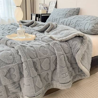 Gray textured blanket draped over a bed with pillows and a small table.