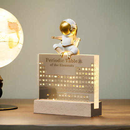 Decorative item with a periodic table design and a small figure on top, illuminated on a wooden surface.