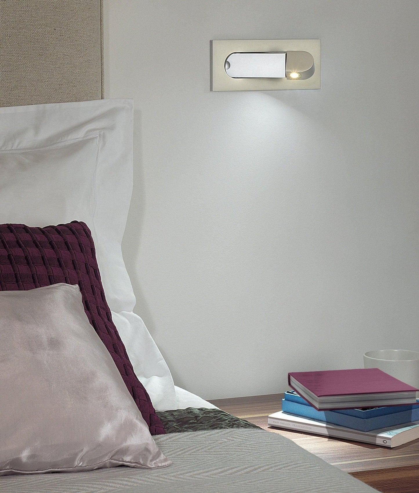 Bedroom setting with a wall-mounted light fixture, books, and pillows.