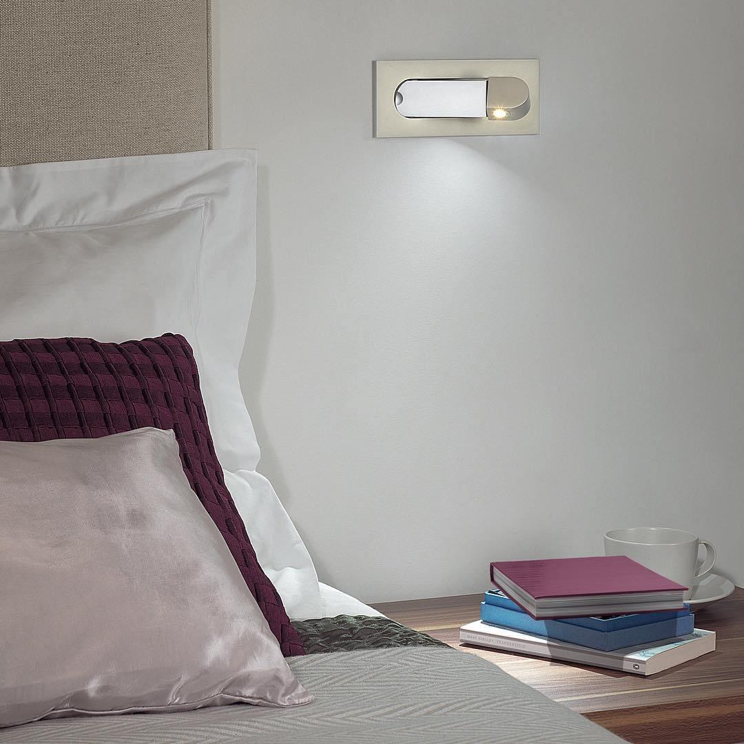 Bedroom scene with pillows, books, and a wall light fixture.