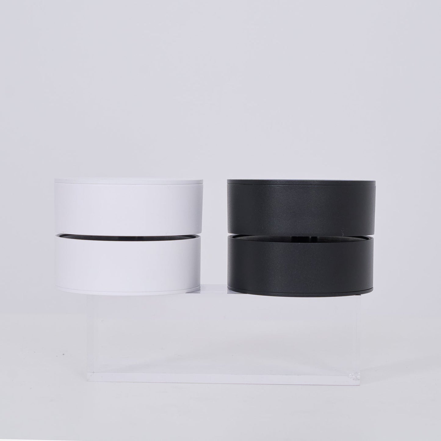 Two cylindrical lamp, one white and one black, on a light gray background.