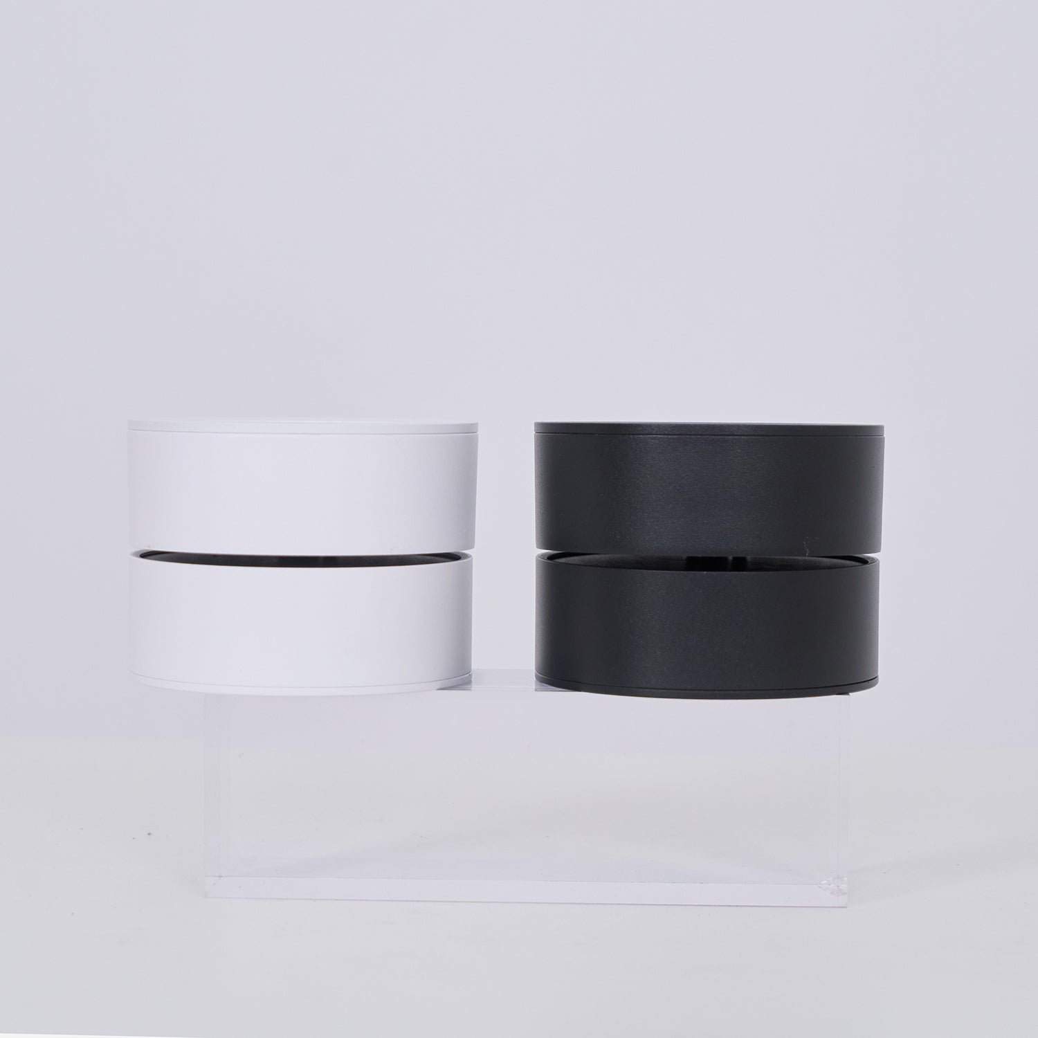 Two cylindrical lamp, one white and one black, on a light gray background.