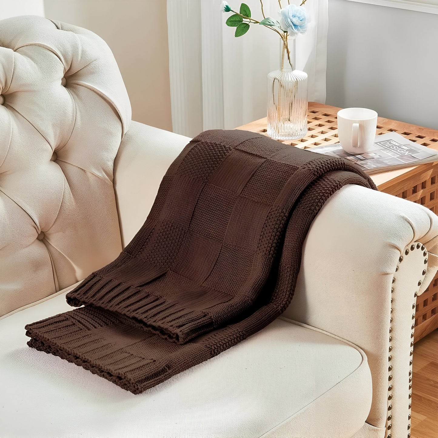 Brown knitted blanket draped over a beige sofa with a side table in the background.