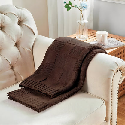 Brown knitted blanket draped over a beige sofa with a side table in the background.