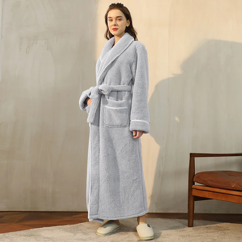 Woman wearing a gray robe standing in a room with a chair and wooden floor.