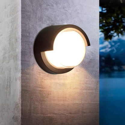 Round outdoor wall light fixture on a concrete wall with blurred natural background