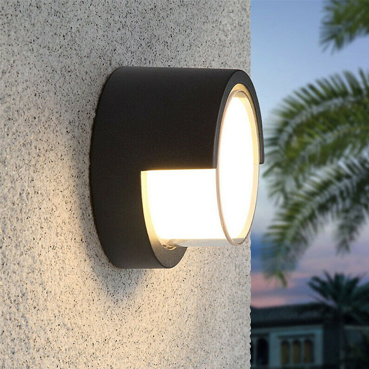 Black outdoor wall light fixture on a textured concrete wall with blurred foliage in the background.