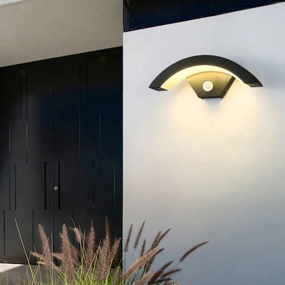 Modern outdoor wall light fixture on a white wall with grass in the foreground.