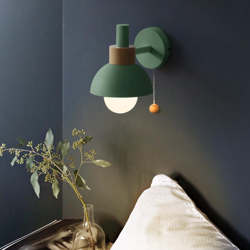 Green wall lamp on a dark wall with a plant and vase in the foreground