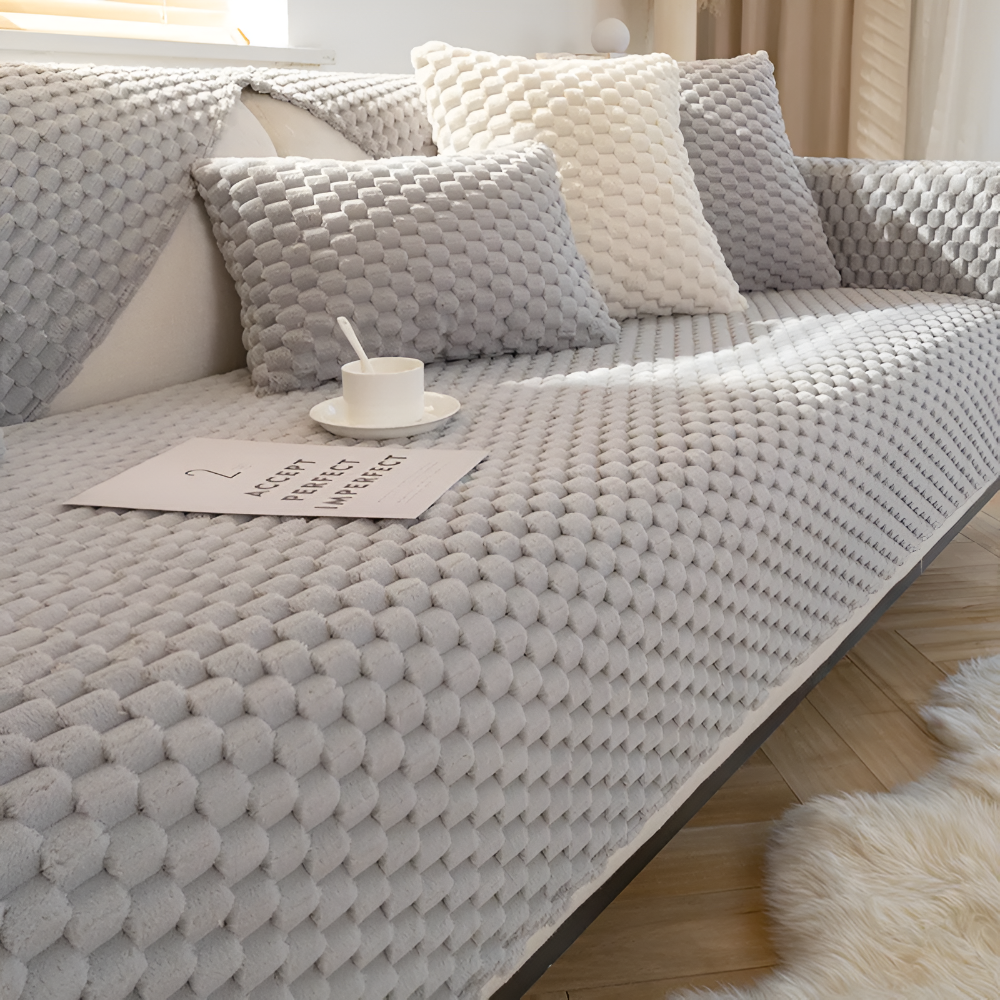 Gray textured sofa with cushions and a cup on a wooden floor.