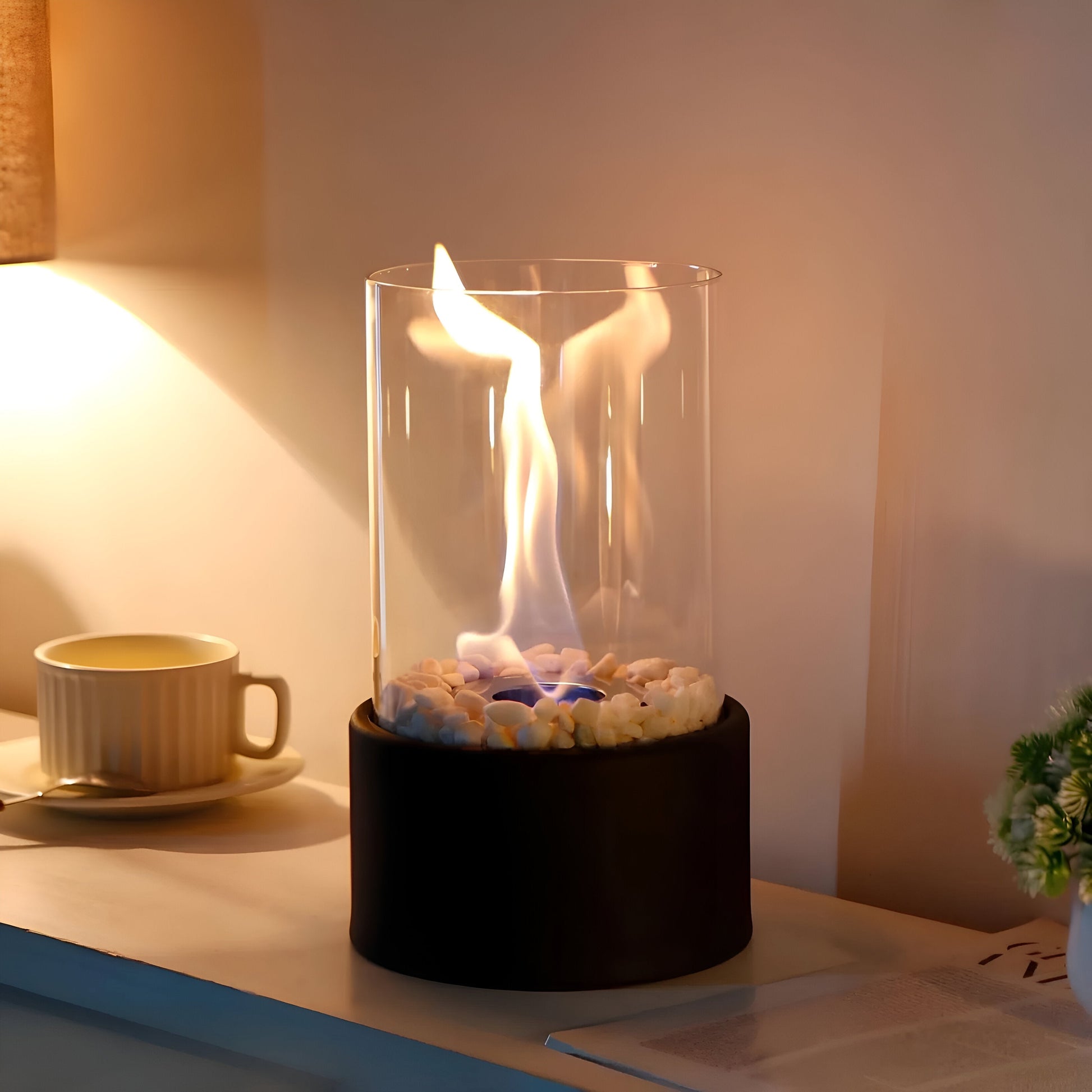Tabletop fire pit with flames on a desk next to a cup and plant