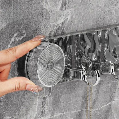 Hand holding a transparent plastic strip with metal hooks against a marble wall.