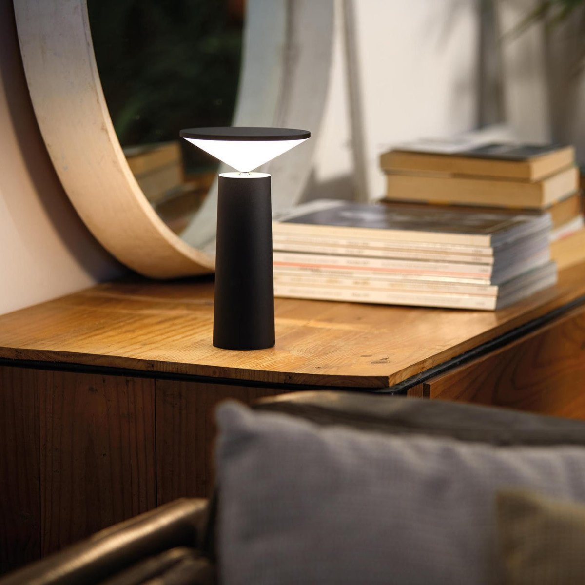 Modern black table lamp on a wooden surface with books and a chair in the background