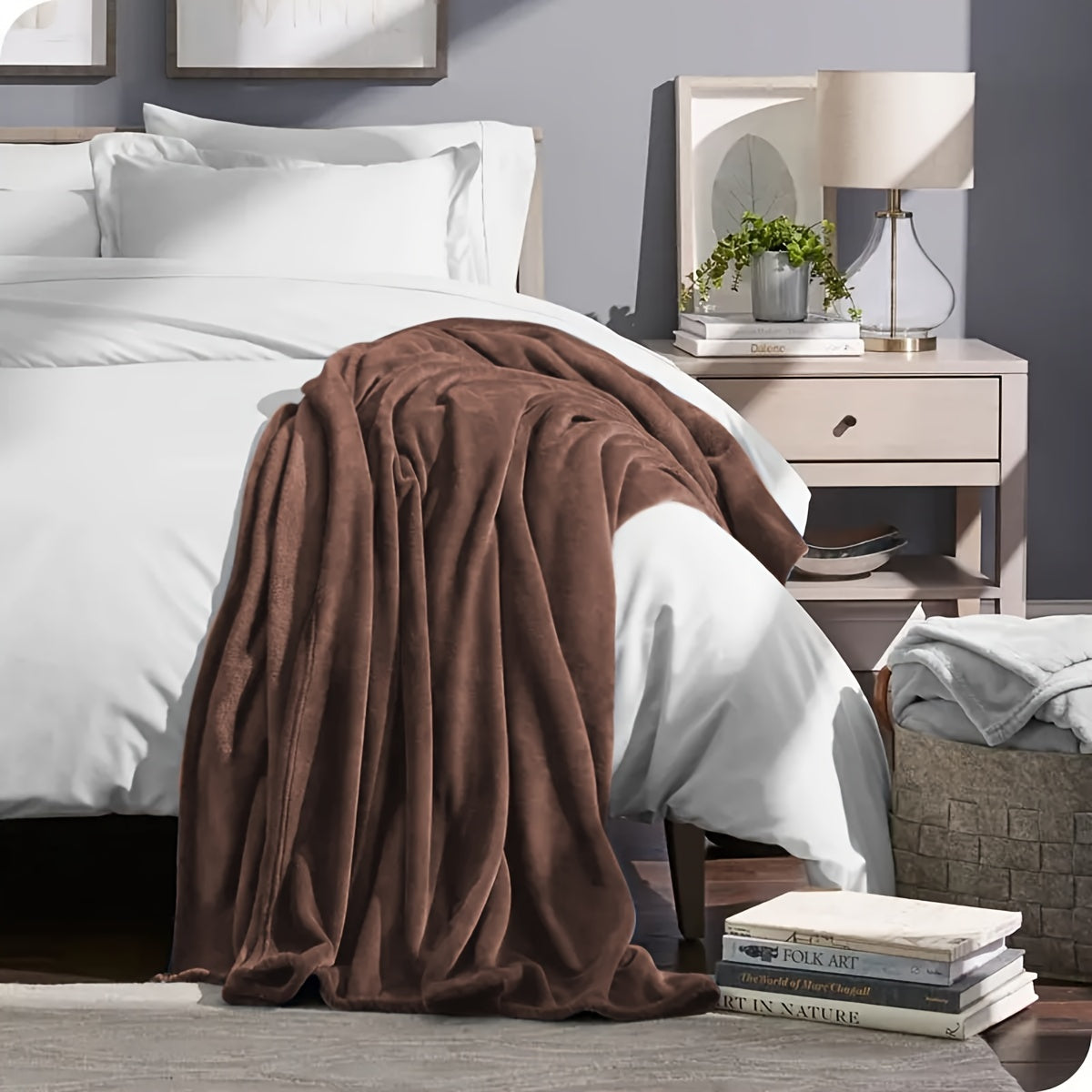 Bedroom with a brown blanket draped over a bed, nightstand with lamp, and books on a shelf.